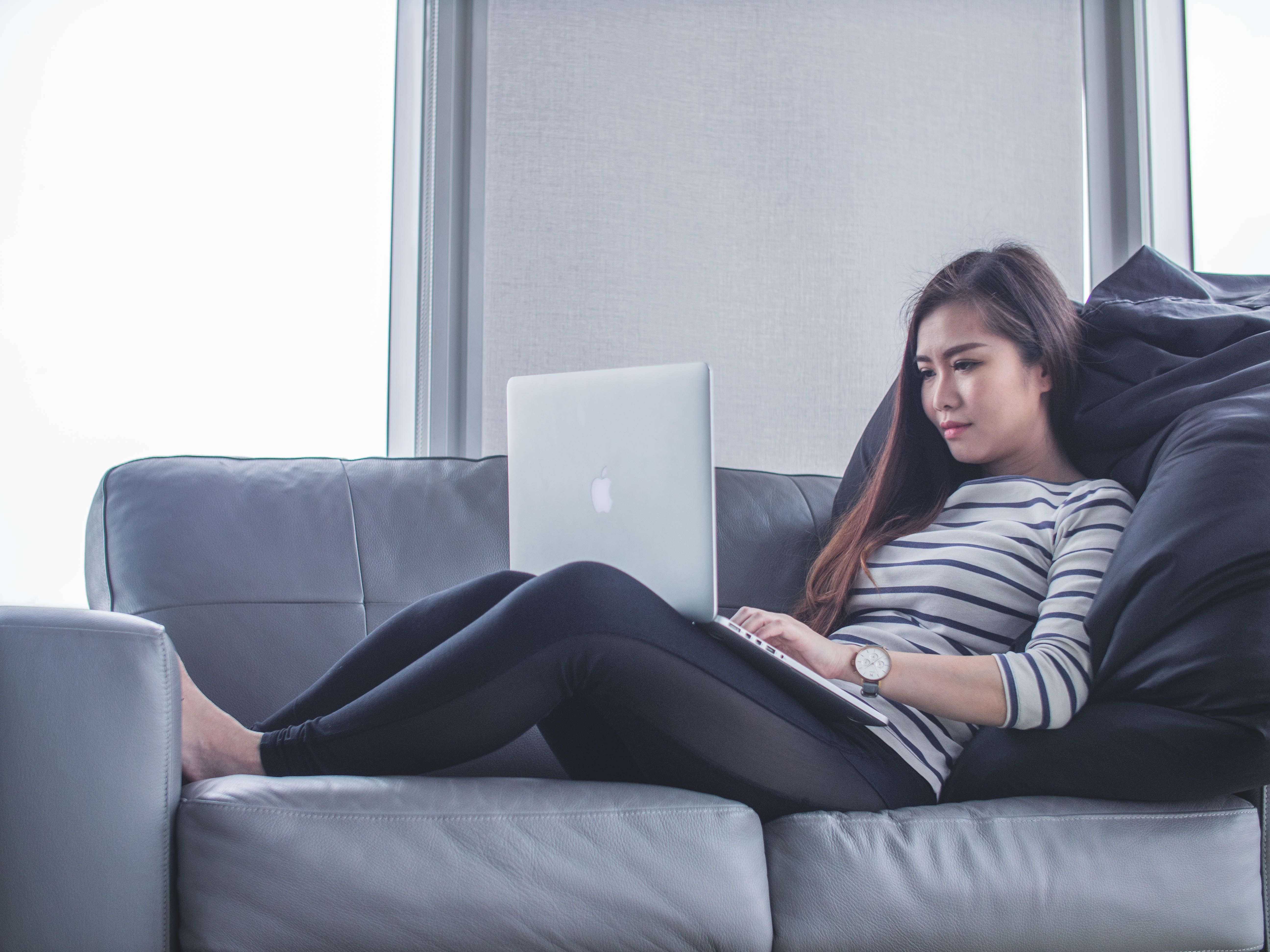 Woman on sofa working with laptop on her lap