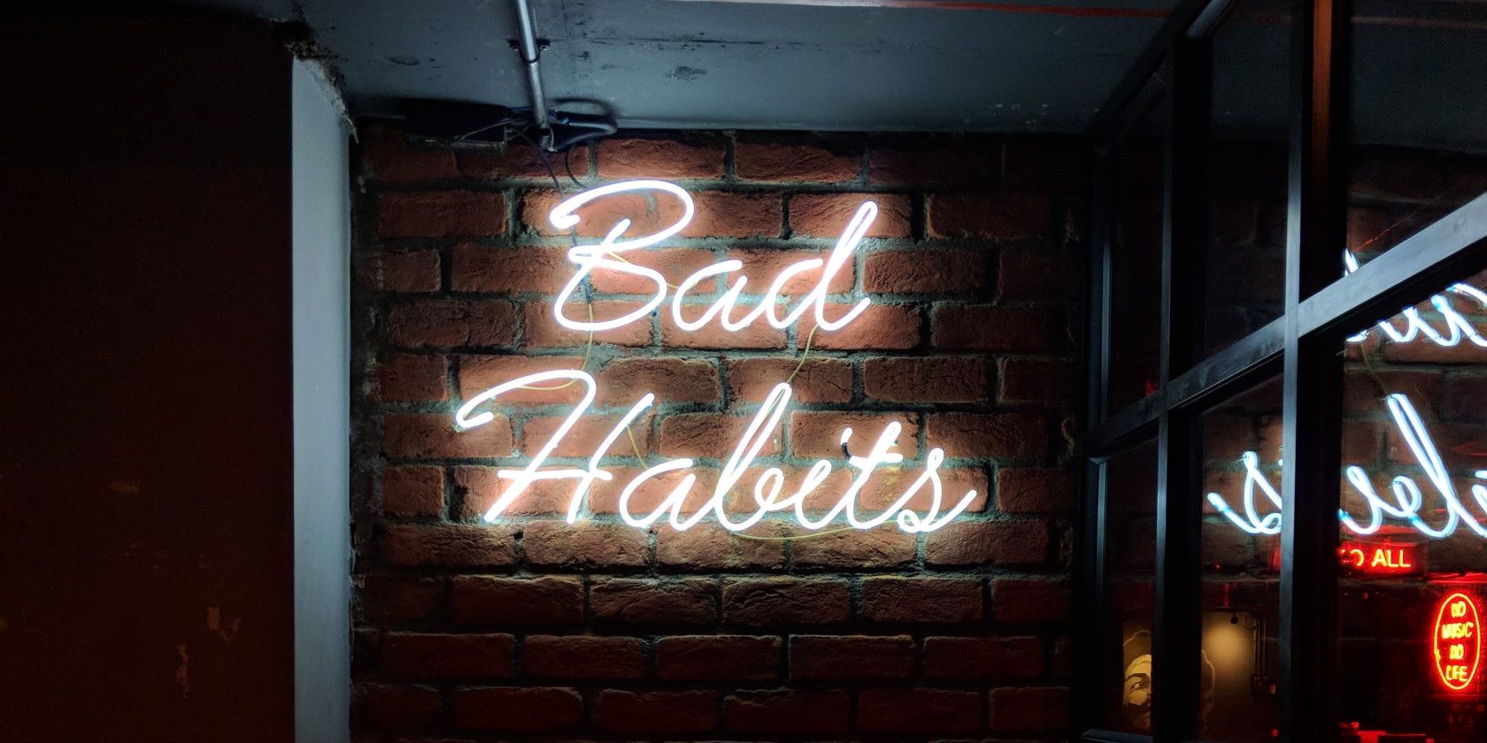 white LED neon sign on brick wall spelling Bad Habits