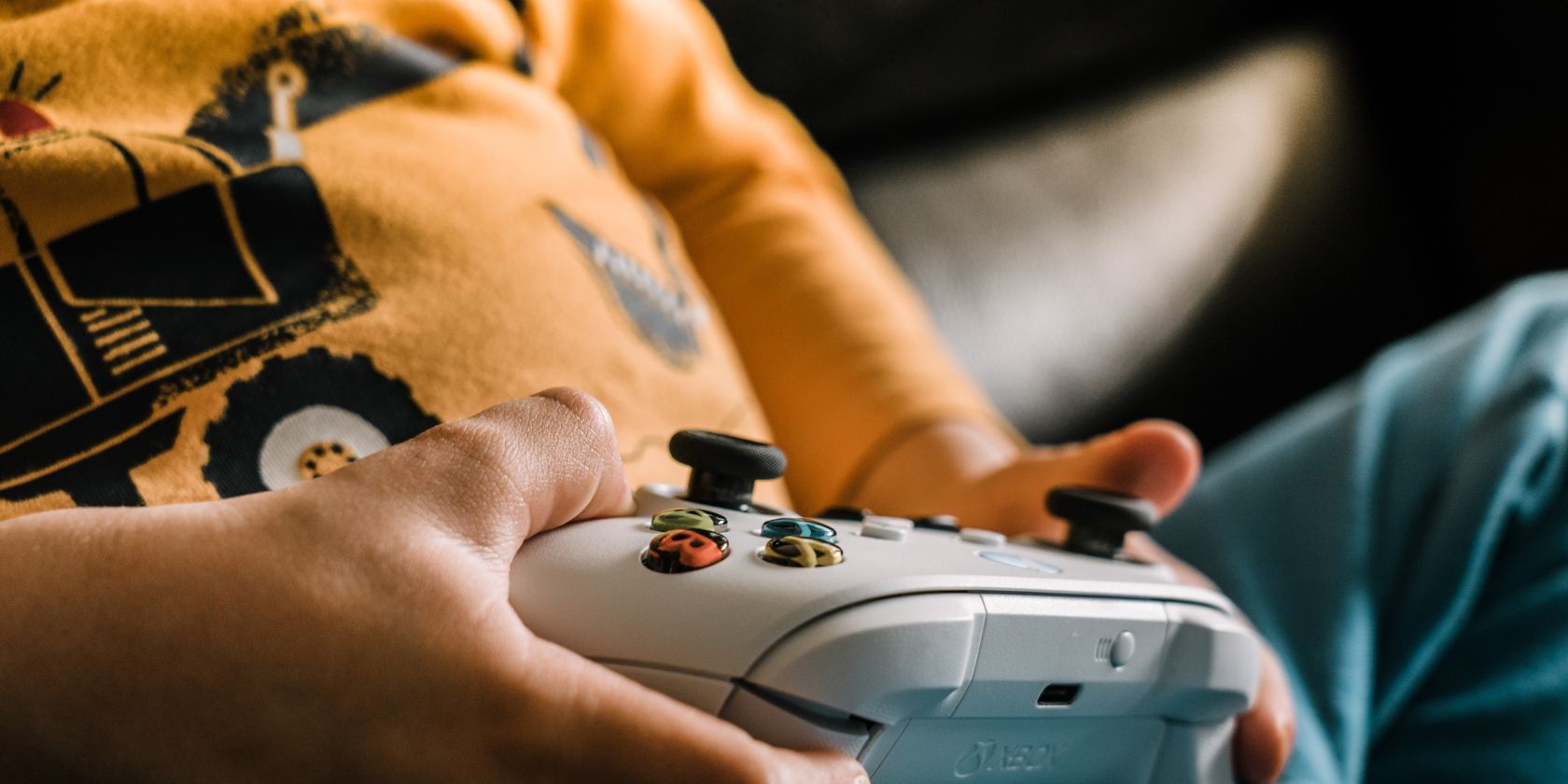 A close up of a child playing Xbox with the controller in their hands assisted by their parent