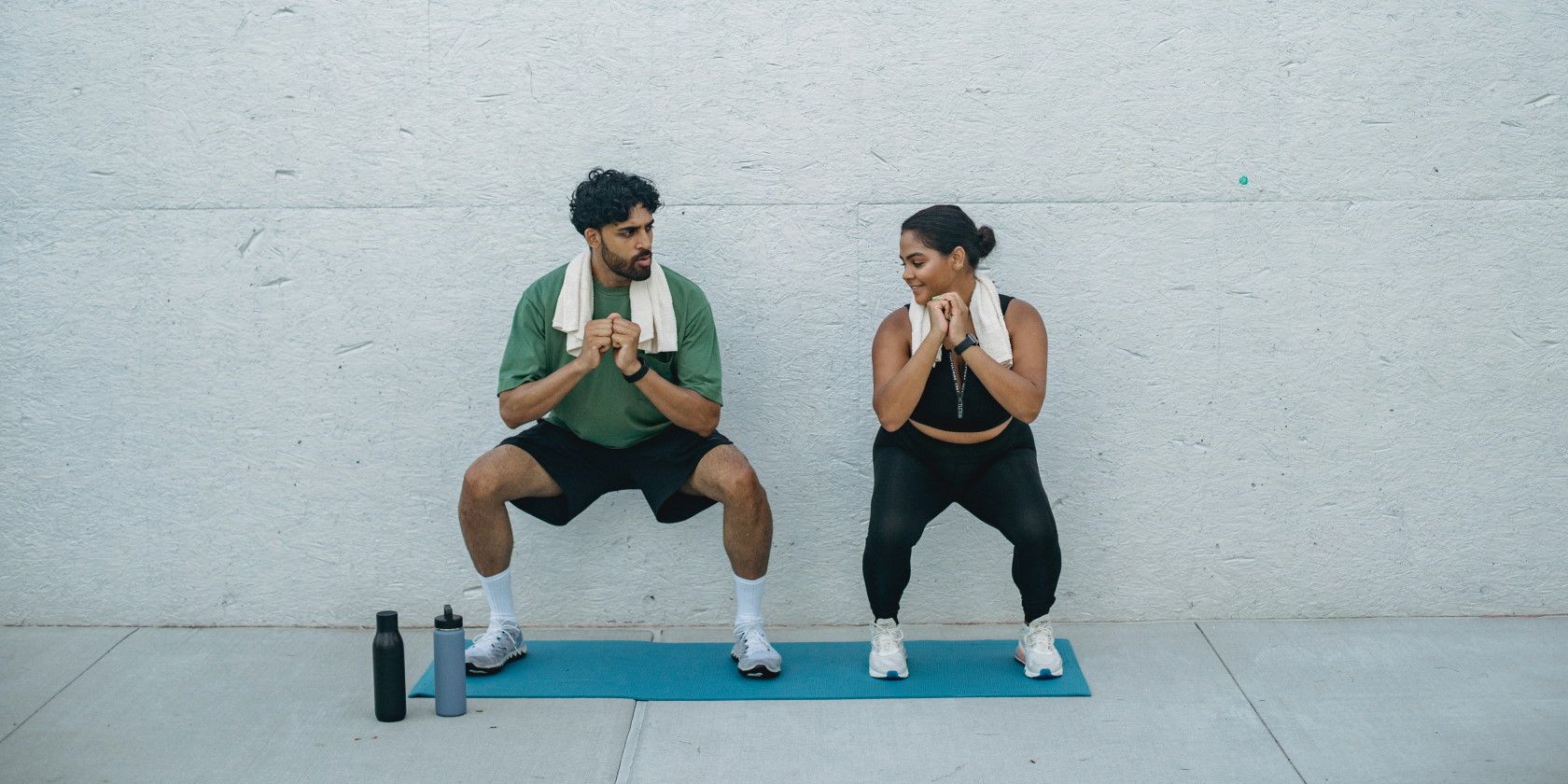 man and woman doing squat exercises against a wall outside