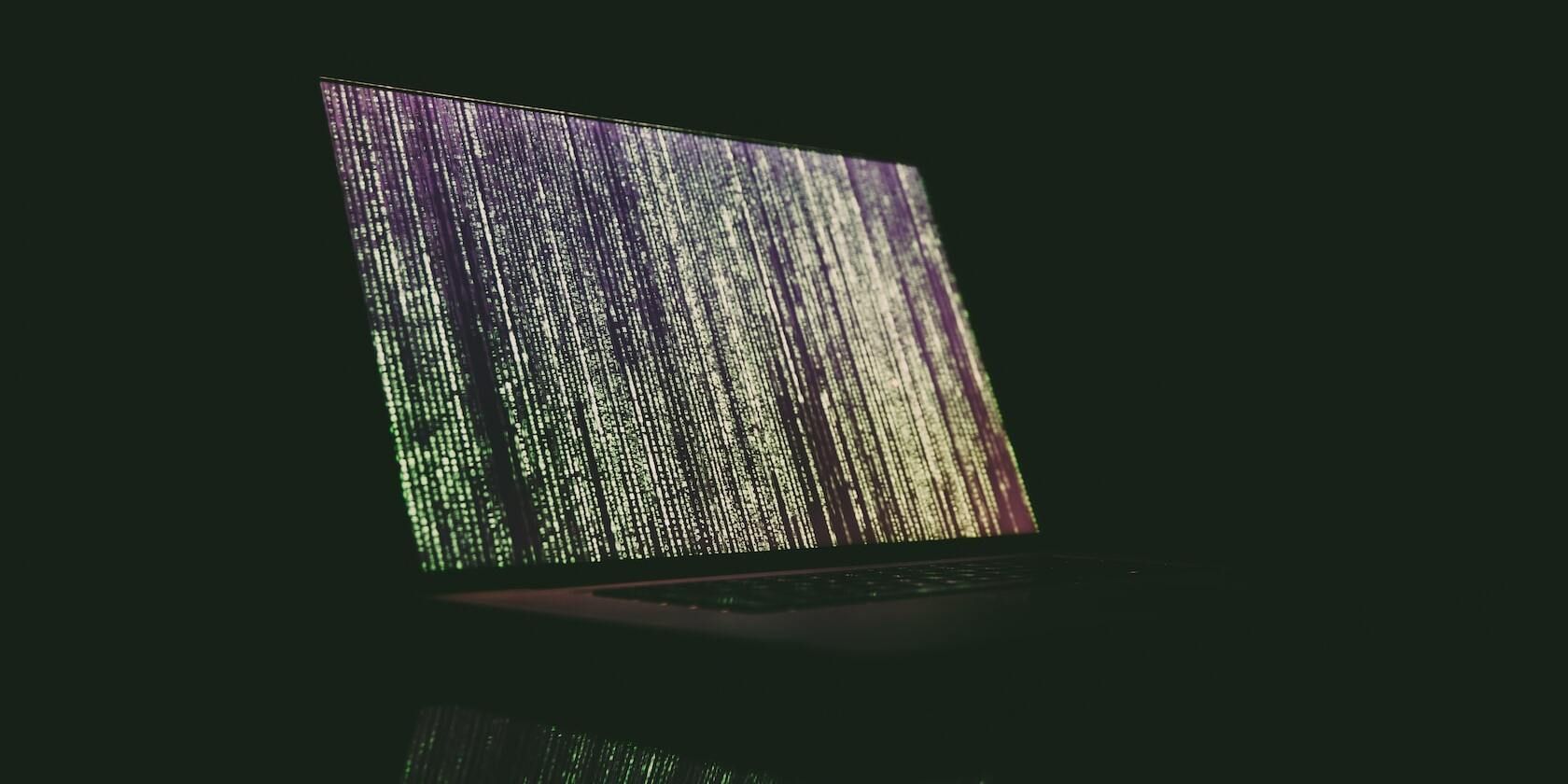 A laptop with green code on the screen in a dark space