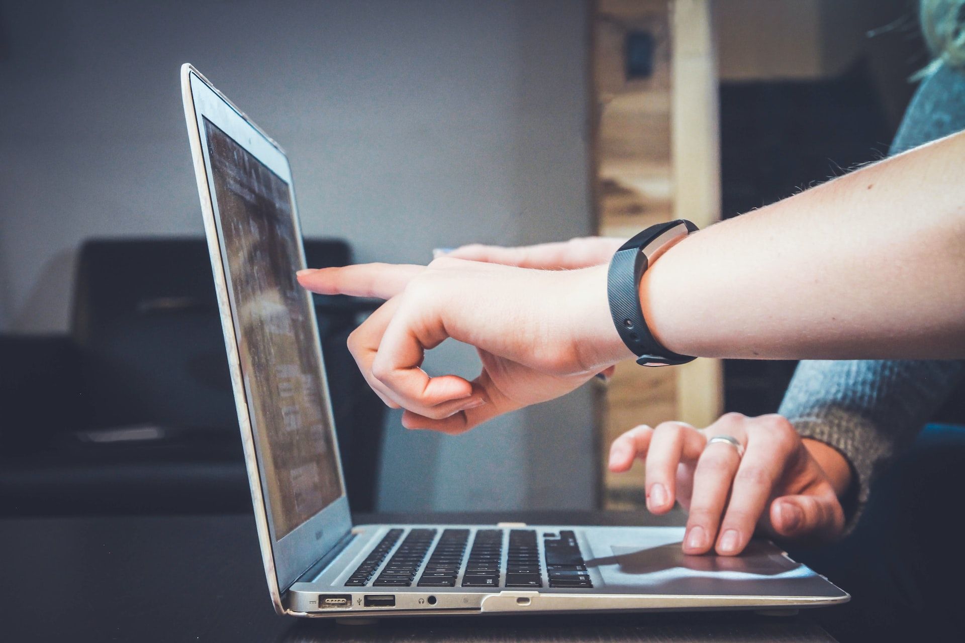 Image of a person wearing a Fitbit band pointing at a laptop