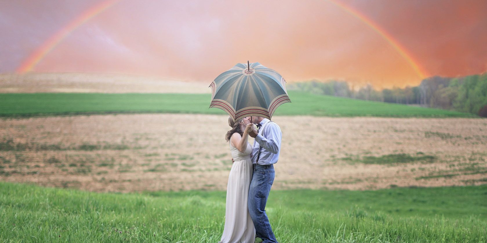Happy couple holding umbrella and kissing outside in front of rainbow