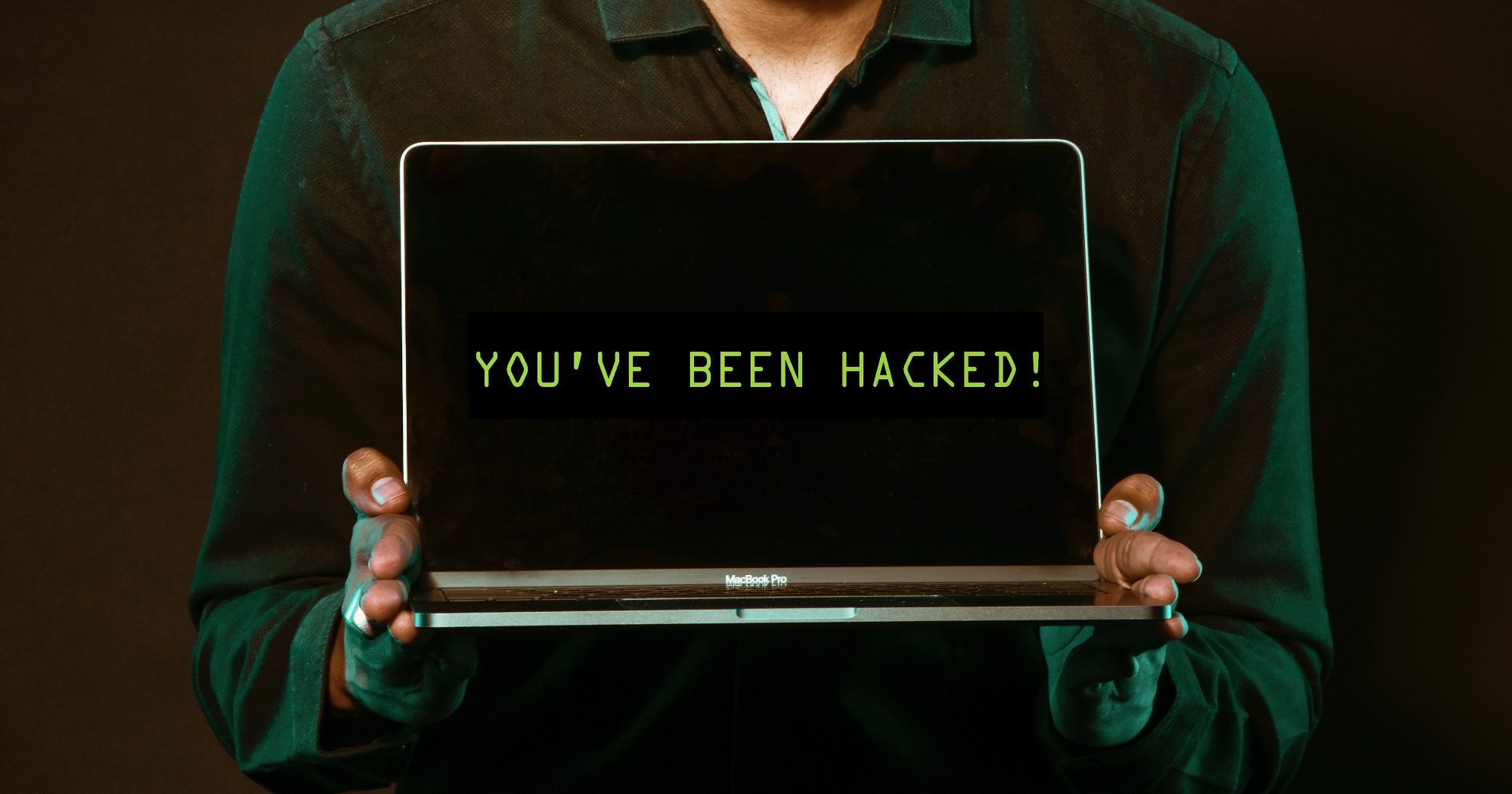 person holding laptop displaying "you've been hacked" on screen
