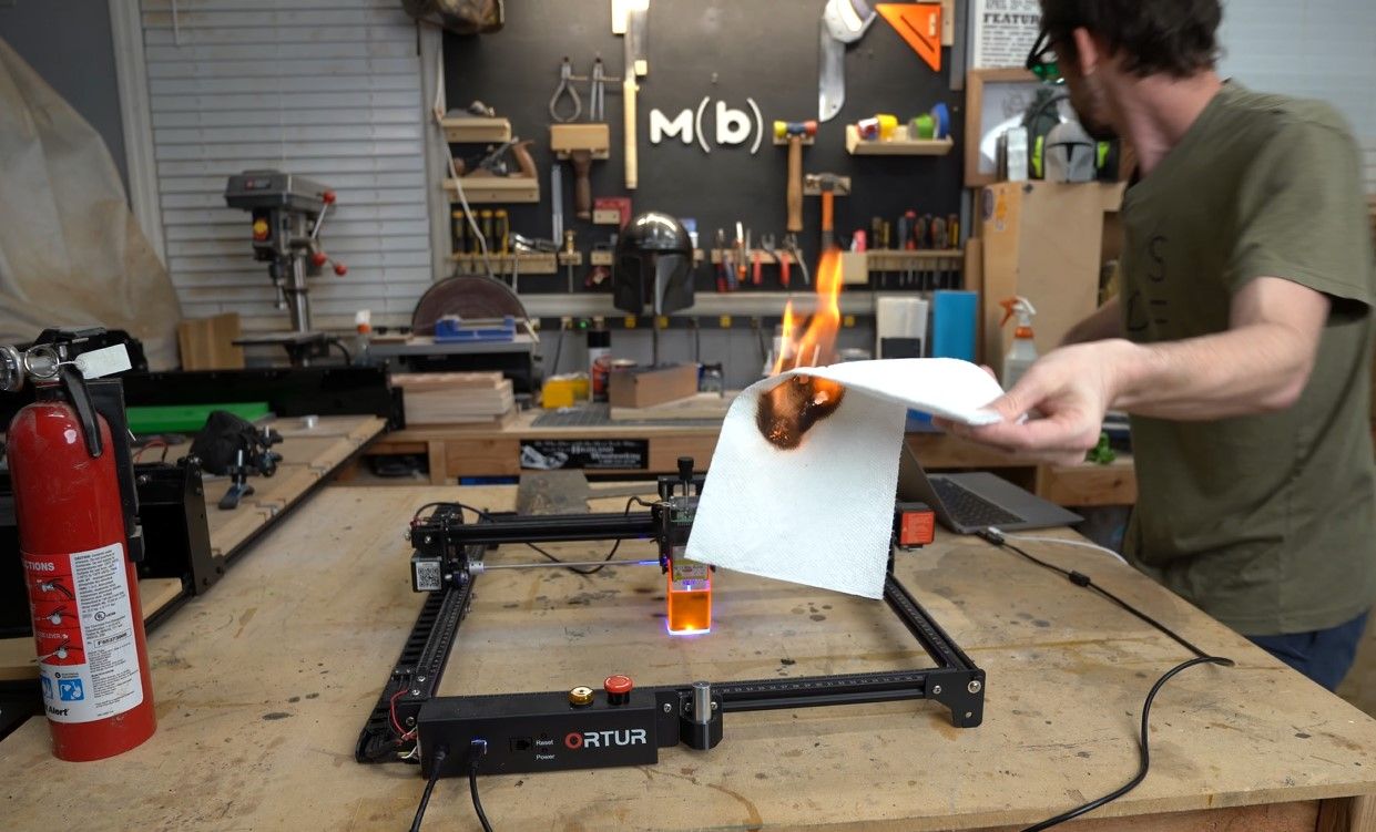 A man holding a paper catching fire after being exposed to a laser cutter