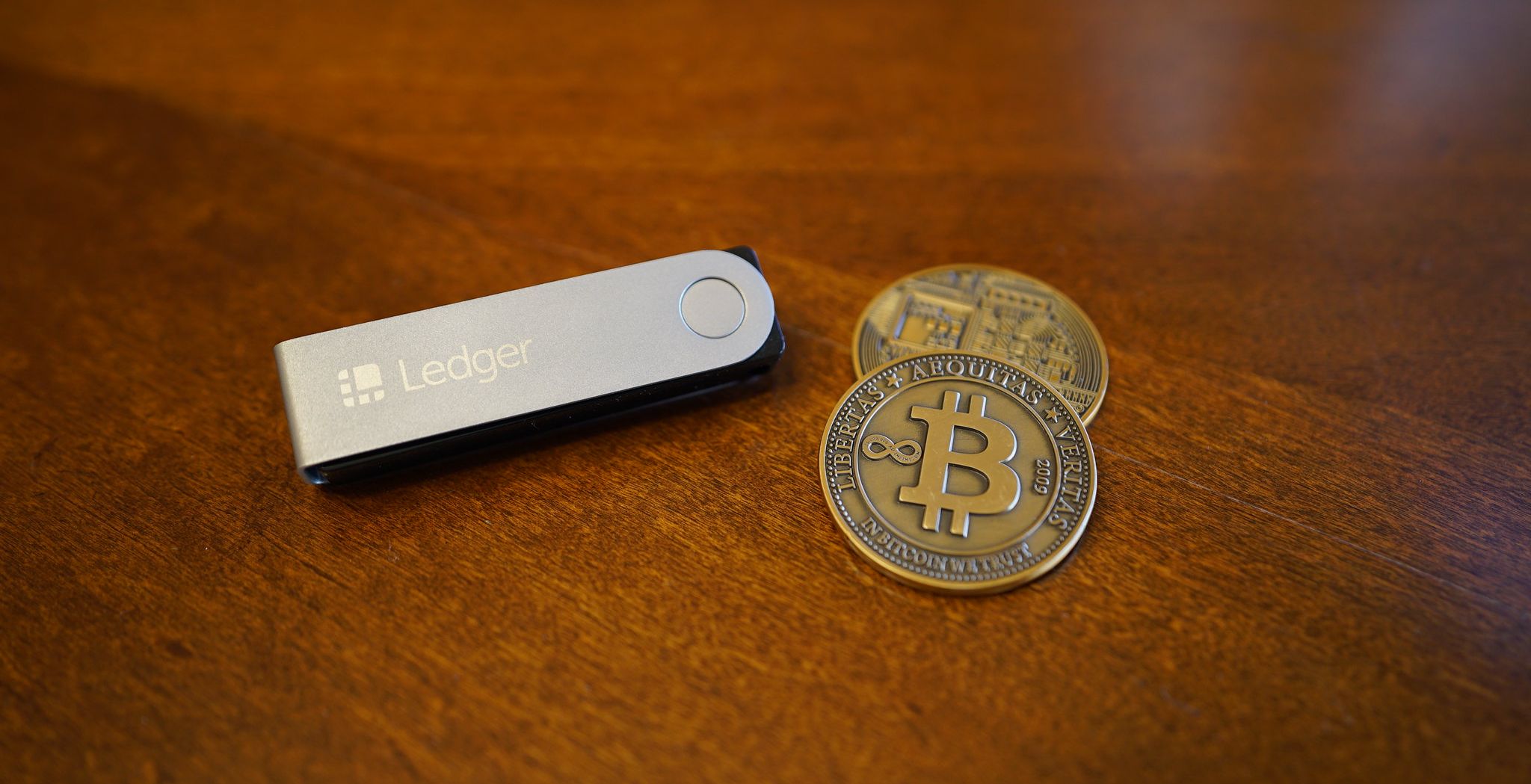 ledger wallet on table next to pair of bitcoins