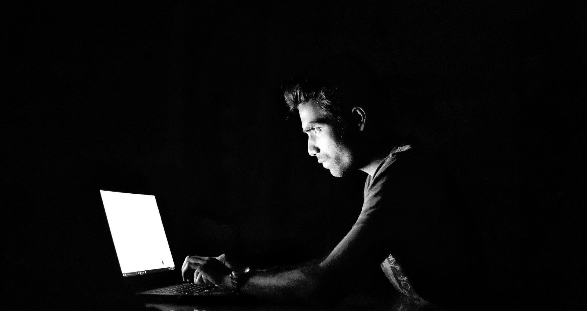 man using laptop in dark room with black and white filter