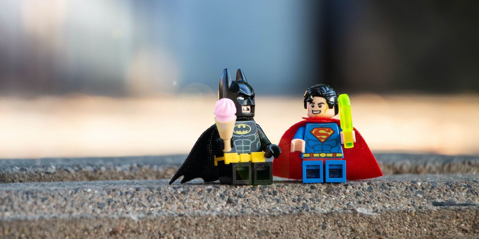 A close-up photo of a Lego Batman and Superman character eating ice cream.