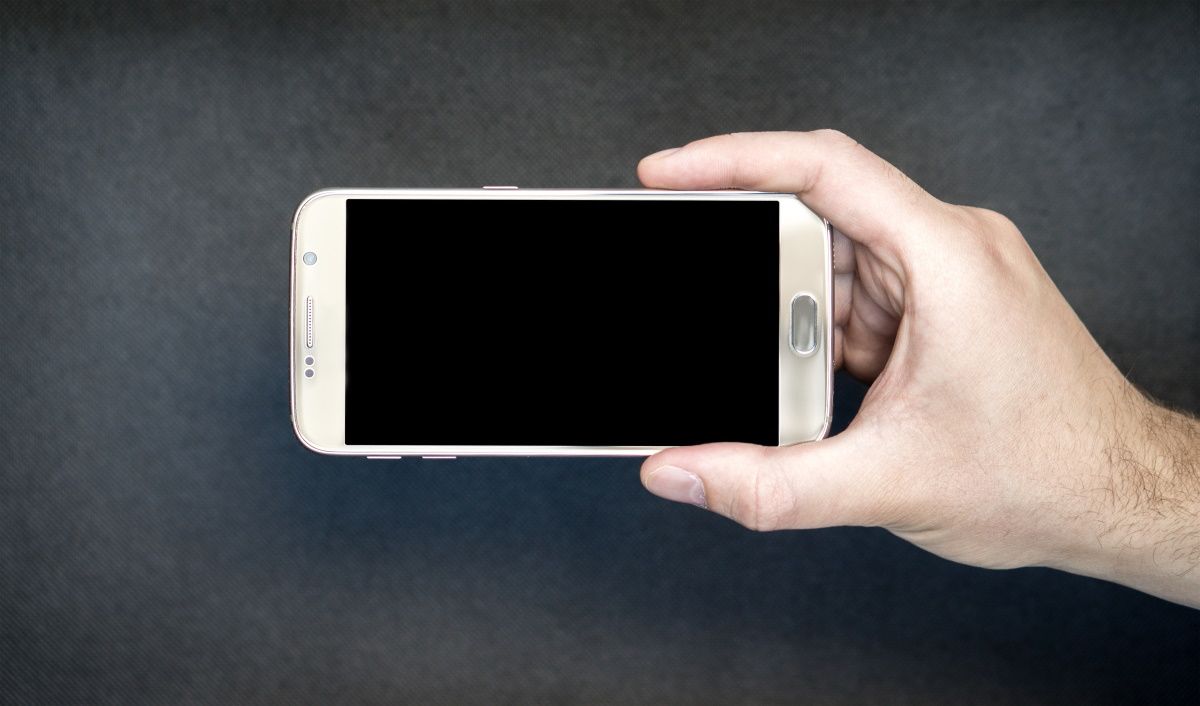 A hand holding a smartphone with the screen turned off