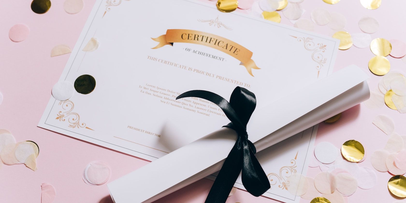 A rolled white paper and certificate on a pink surface