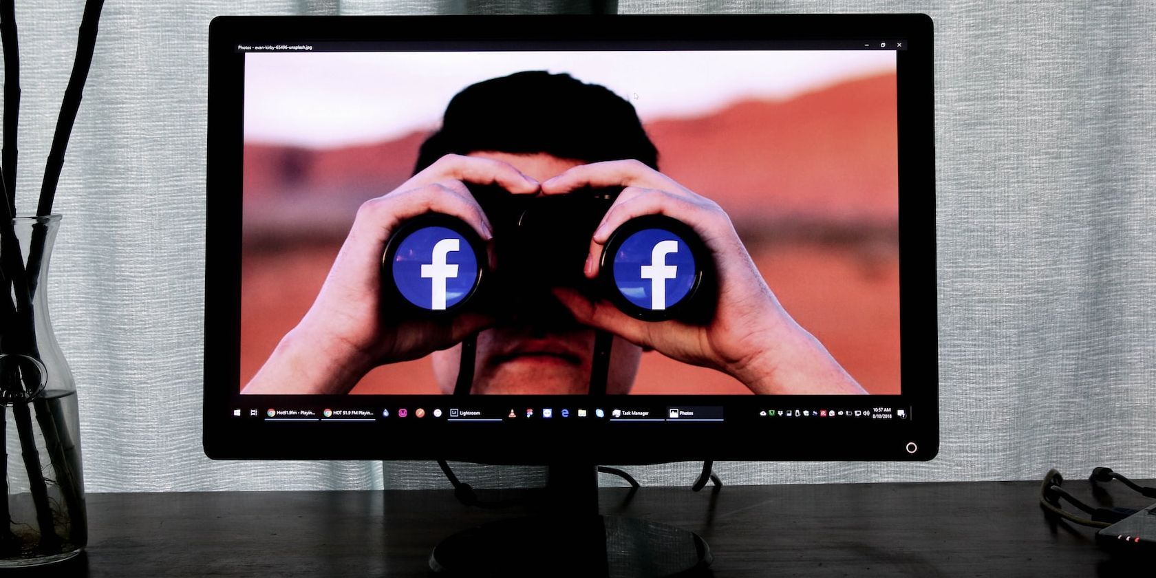 Desktop Monitor Placed on a Table Showing Image of a Man Viewing From a Binocular Covered With Facebook Logo Icons