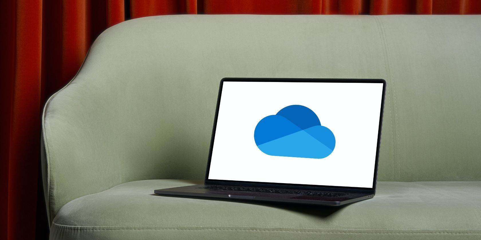 A black laptop placed on a sofa with a OneDrive logo open on it