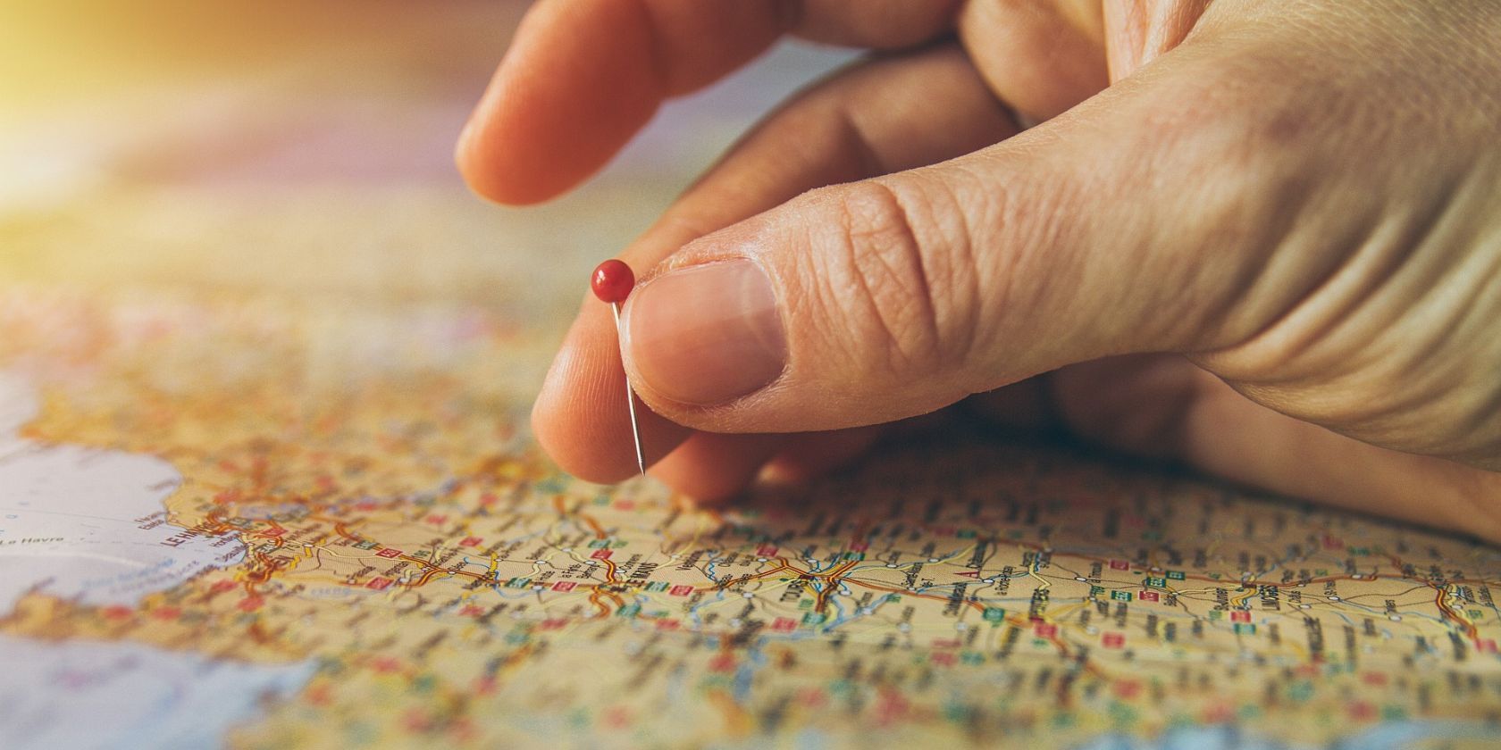 Bir dünya haritasının yüzeyine kırmızı bir raptiye yerleştiren bir elin yakın çekimi