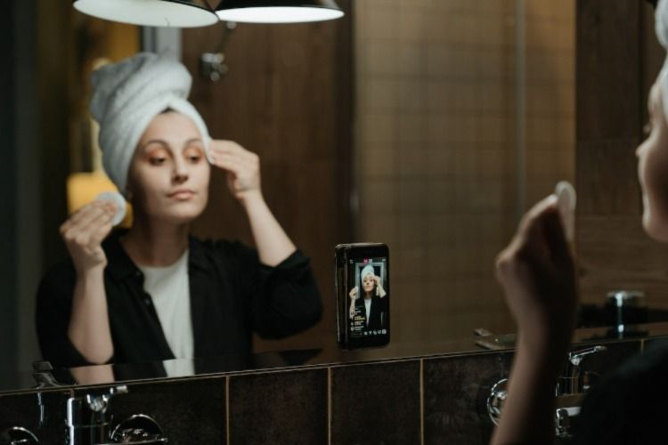 Woman putting make up on in front of mirror with a phone
