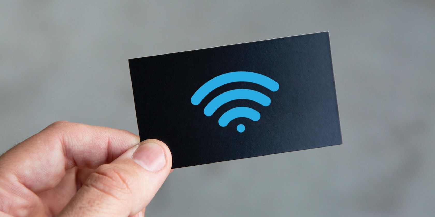 A hand holds a black business card that has a blue wireless symbol on it.