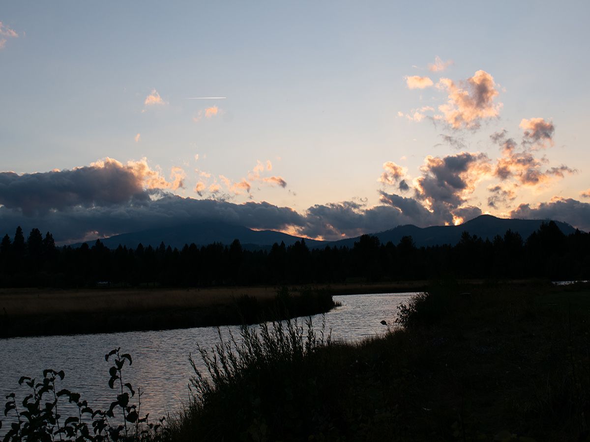 Matahari terbenam di atas sungai dengan latar depan gelap dari kamera sensor crop.