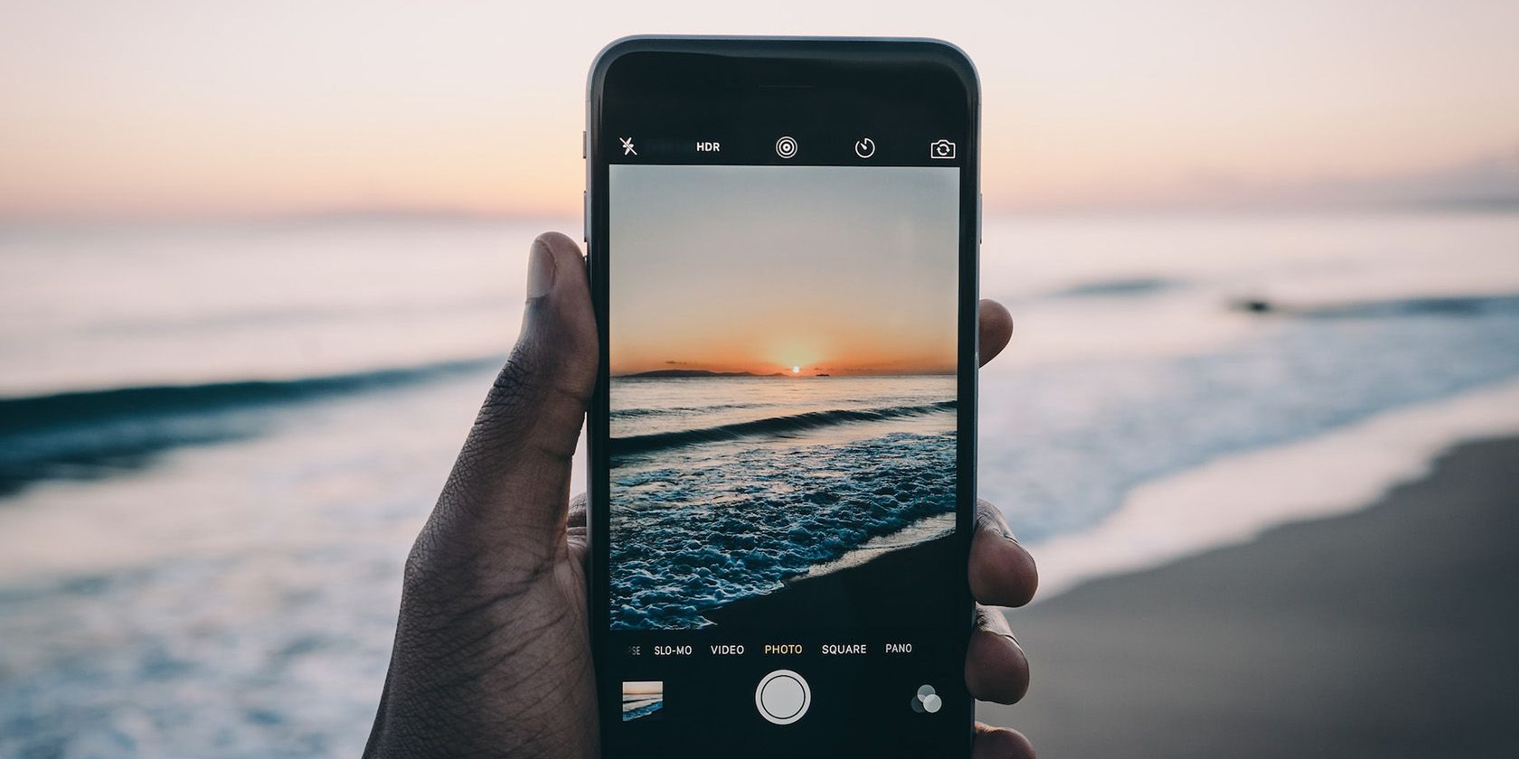 A hand taking holding an iPhone taking a picture of the ocean