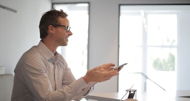 Man sitting in front of a laptop smiling and holding his phone