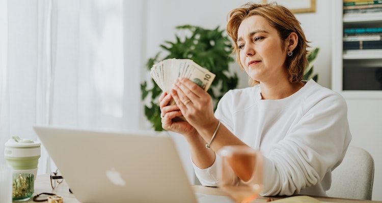 Woman sitting in front of a laptop with cash in her hands
