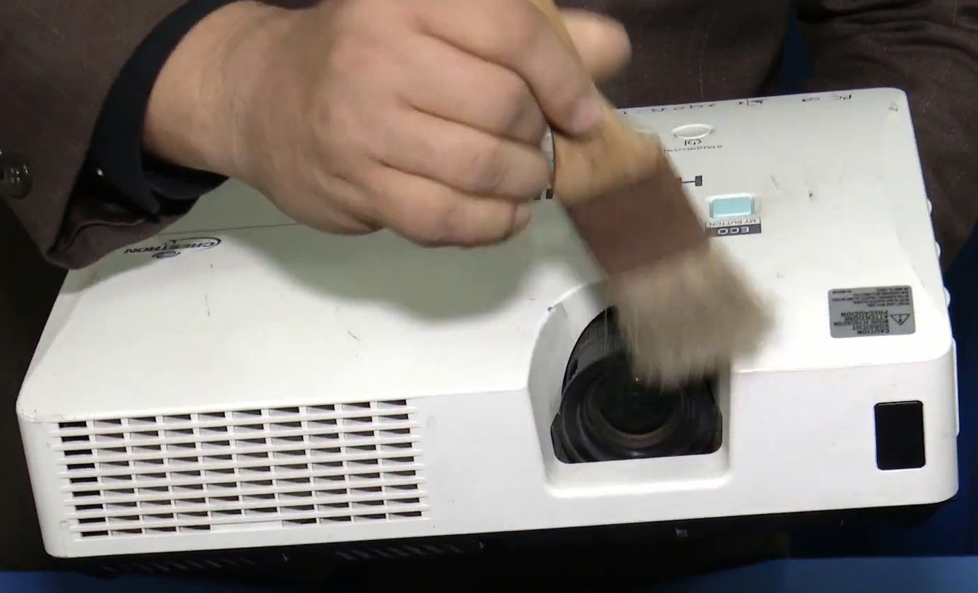 Hand of a white man wiping the lens of a projector using a brush