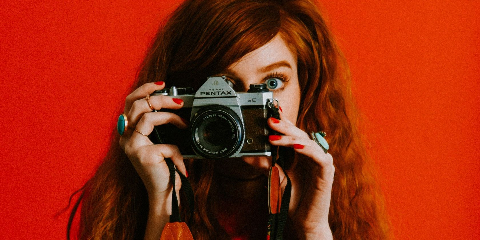 Woman Wearing Red Against Red Background Taking Picture With Camera