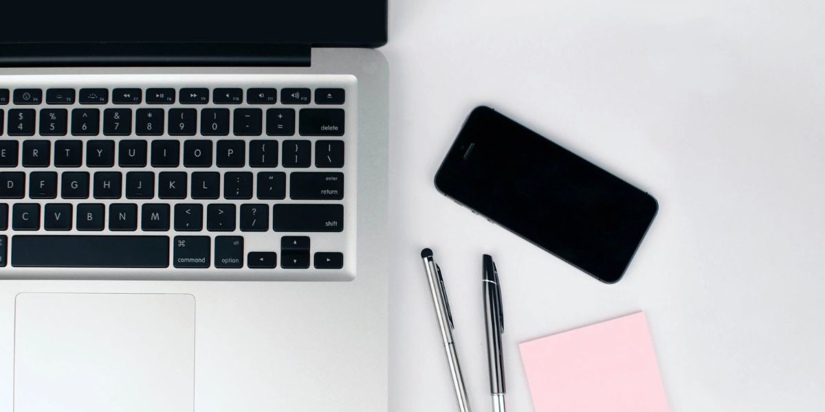 iphone placé sur un tableau blanc à côté d'un macbook, de stylos et d'un post-it rose