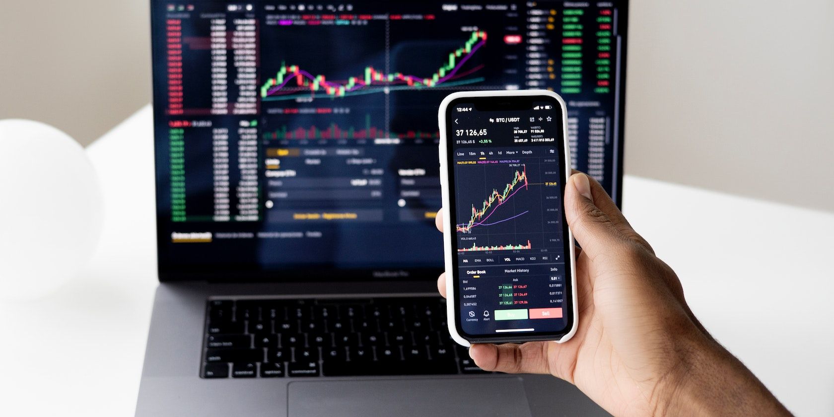 A person holding a smartphone showing live trading graphs_