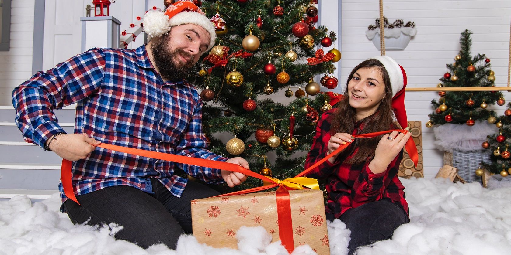 A couple in a Christmas decorated room unwrapping a gift