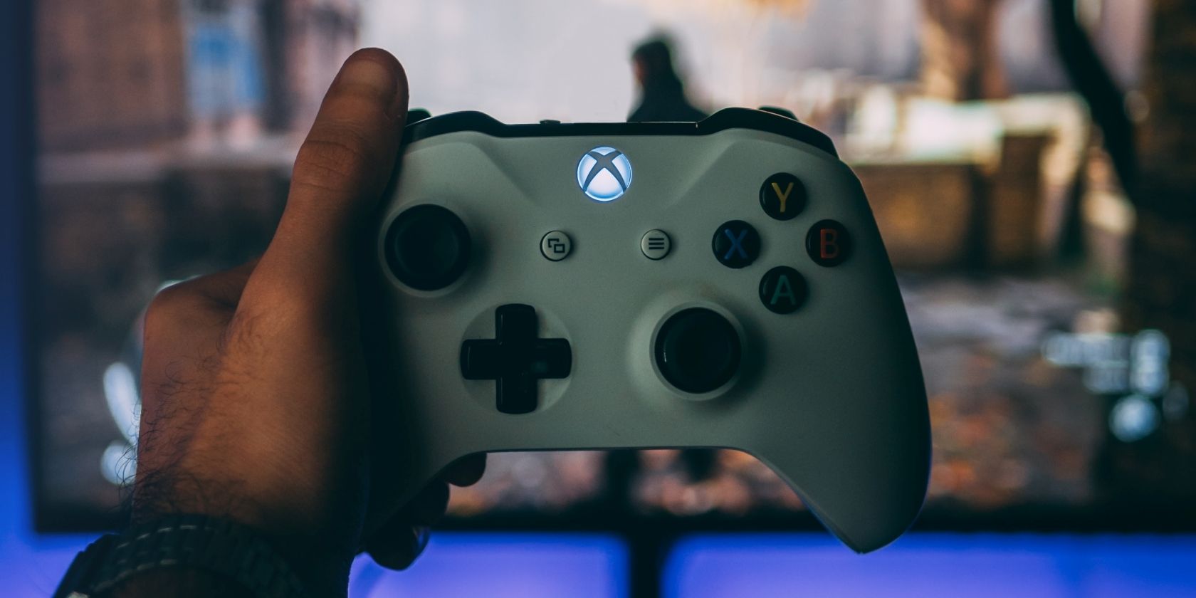A picture of a man holding up a white Xbox One controller in front of a monitor