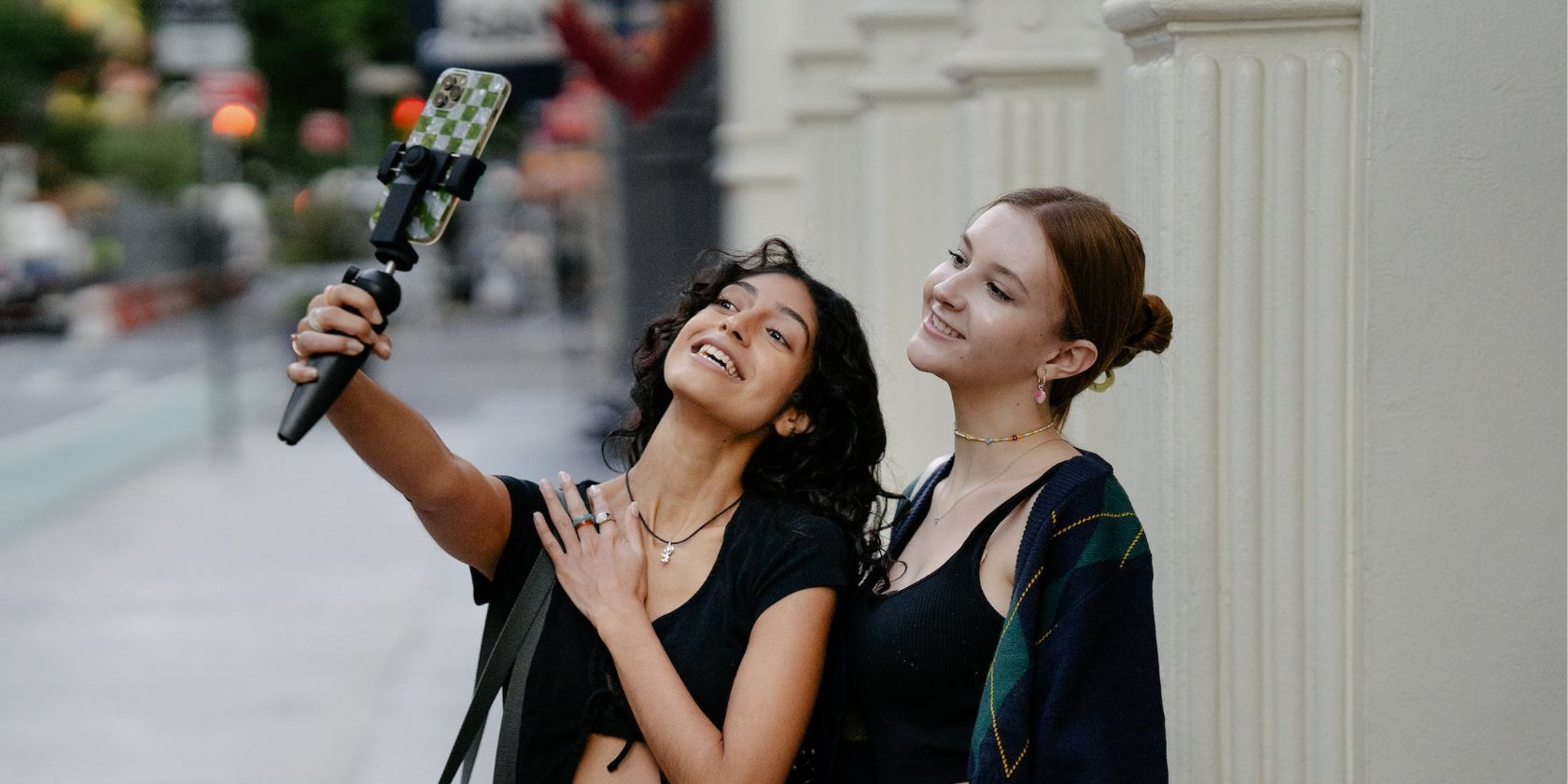 two women smiling and taking a selfie together on iphone using a short selfie stick 