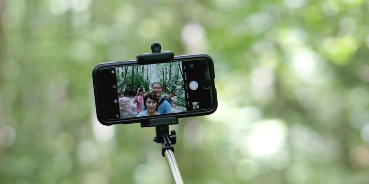 two people taking picture in forest using iphone secured on selfie stick