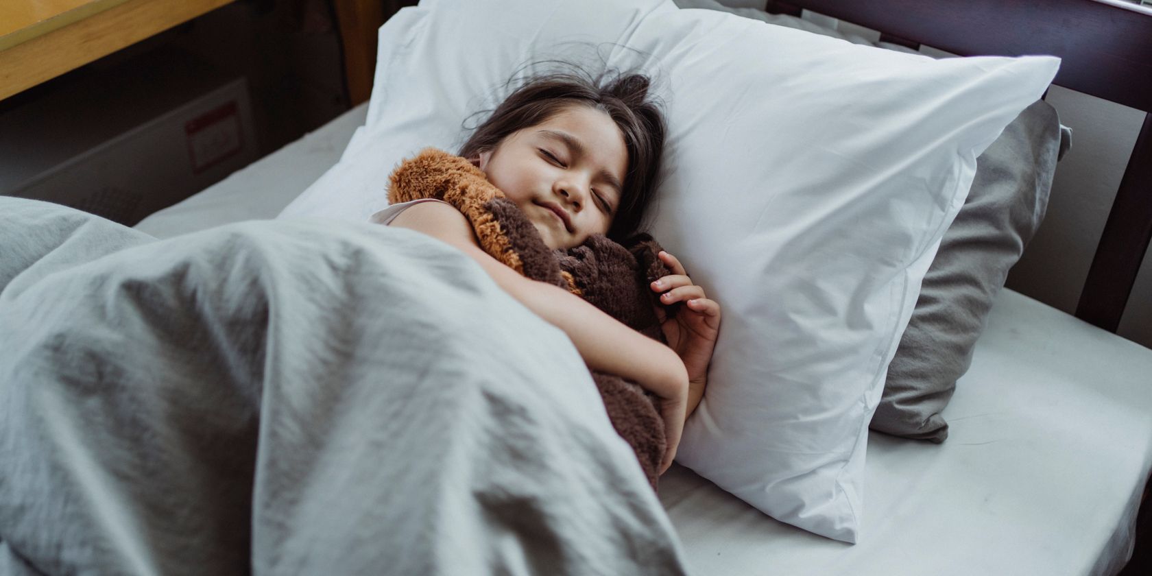 a child asleep in bed cuddling a teddy bear