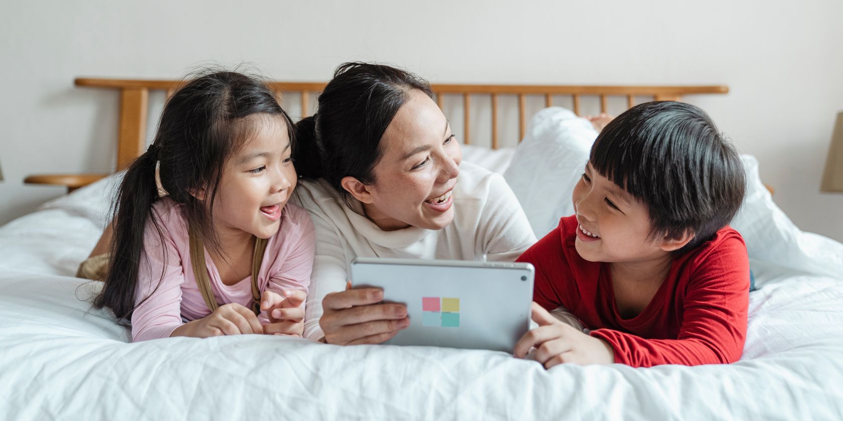 a happy family use a tablet lying on a bed