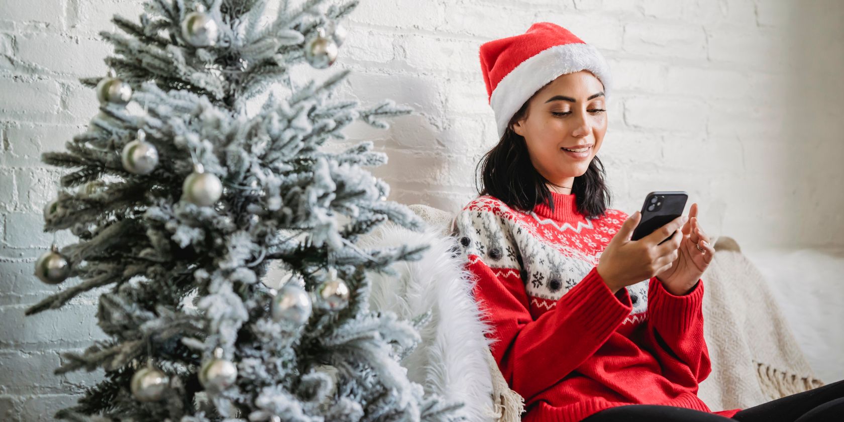 a lady sits next to a Christmas tree looking at a phone