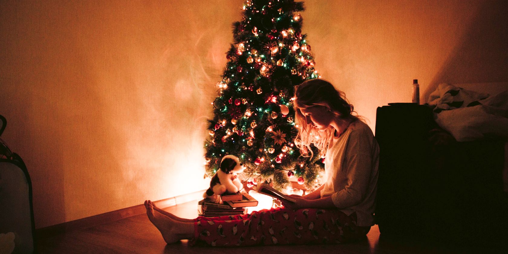a lady sits next to a Christmas tree reading a book