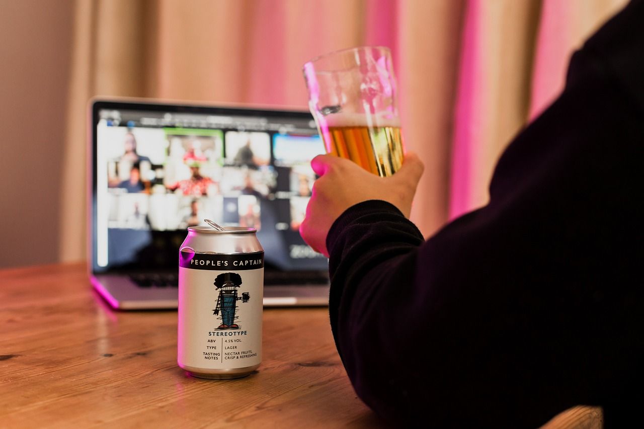A person sitting in front of an online meeting with a can of beer