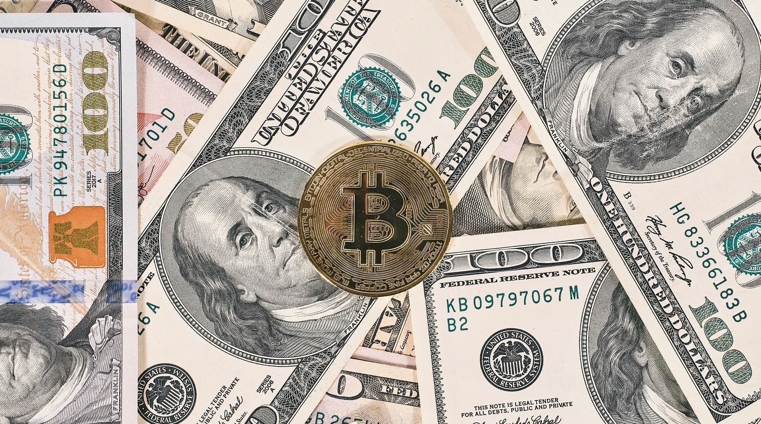 single bitcoin on top of hundred dollar bills