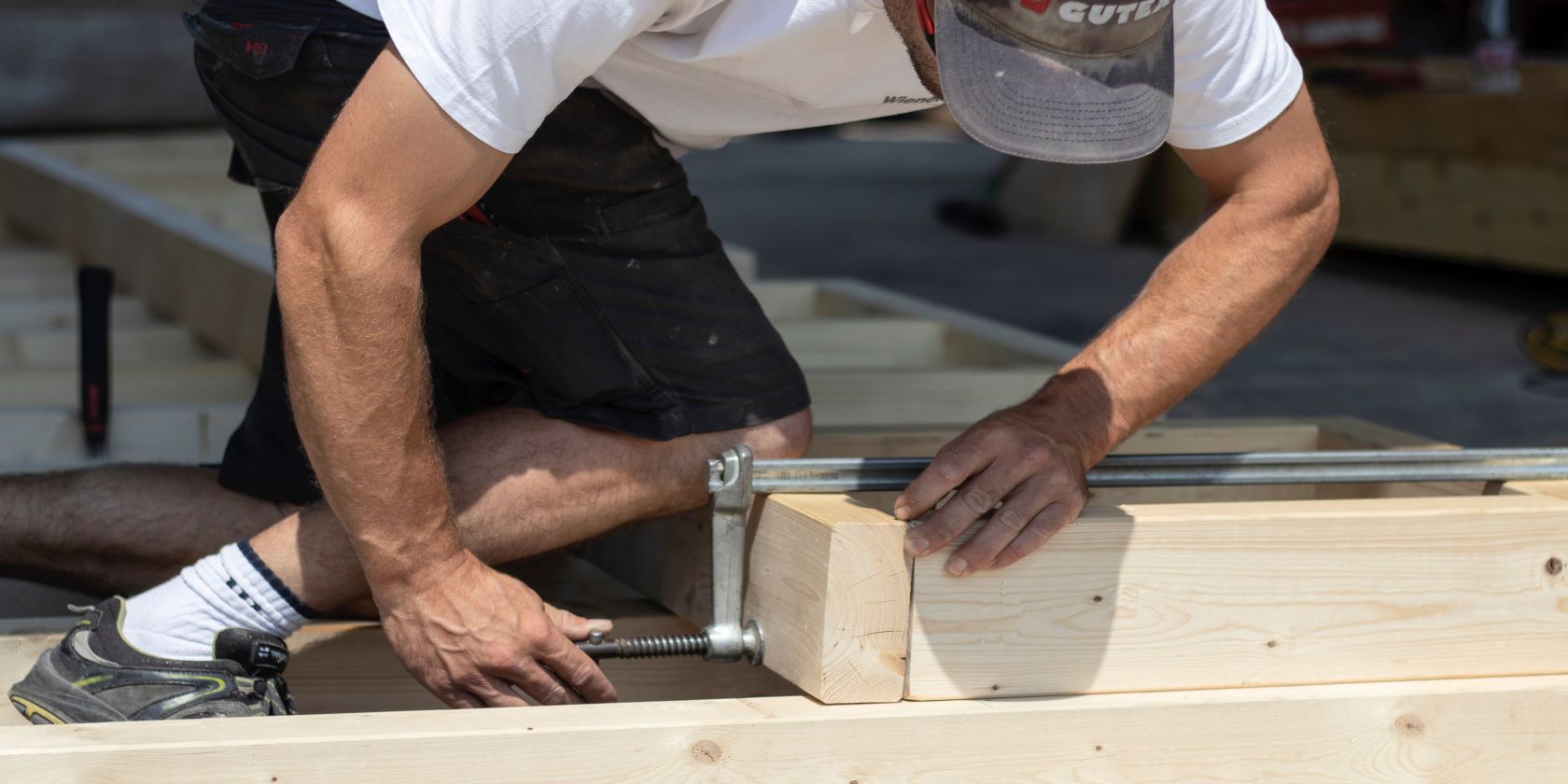 A builder holding two pieces of wood together with a metal clamp