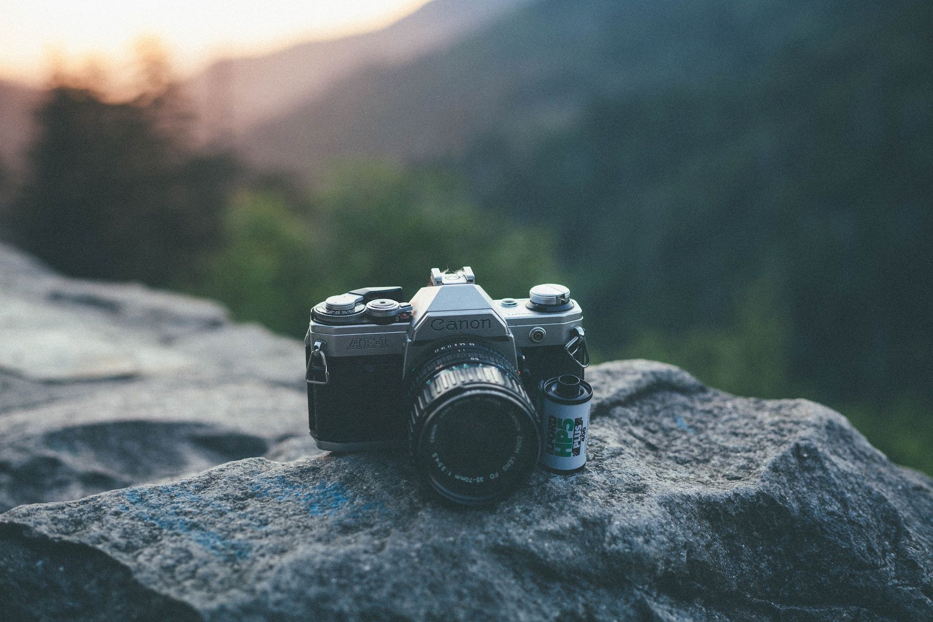 canon ae1 sitting on rock next to a roll of film