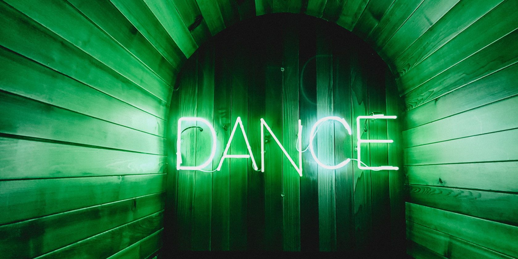 neon green sign on wooden wall spelling dance