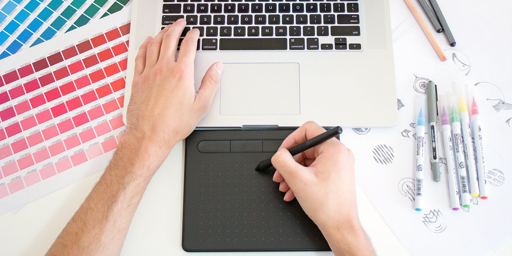 graphic designer working with a trackpad, macbook, and pantone colors