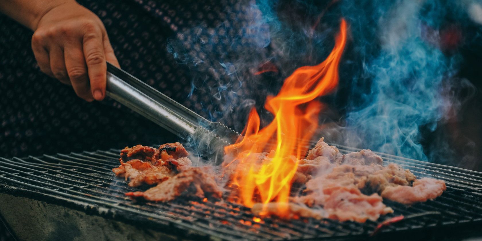 close-up of person grilling meat over flames