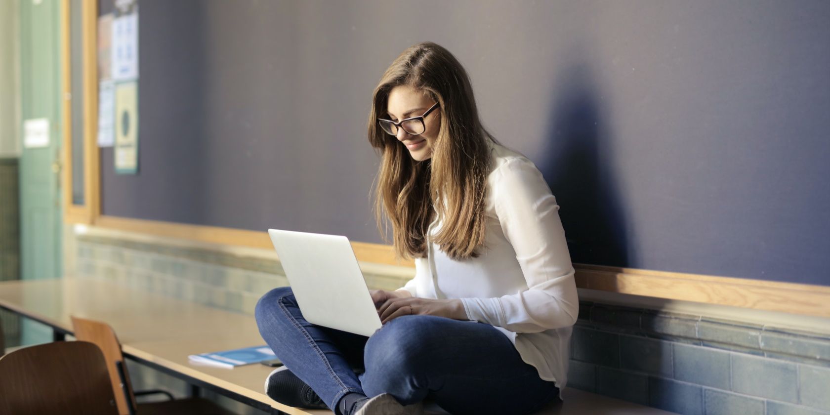 Femme souriante utilisant un ordinateur portable et assise sur une table dans une salle de classe