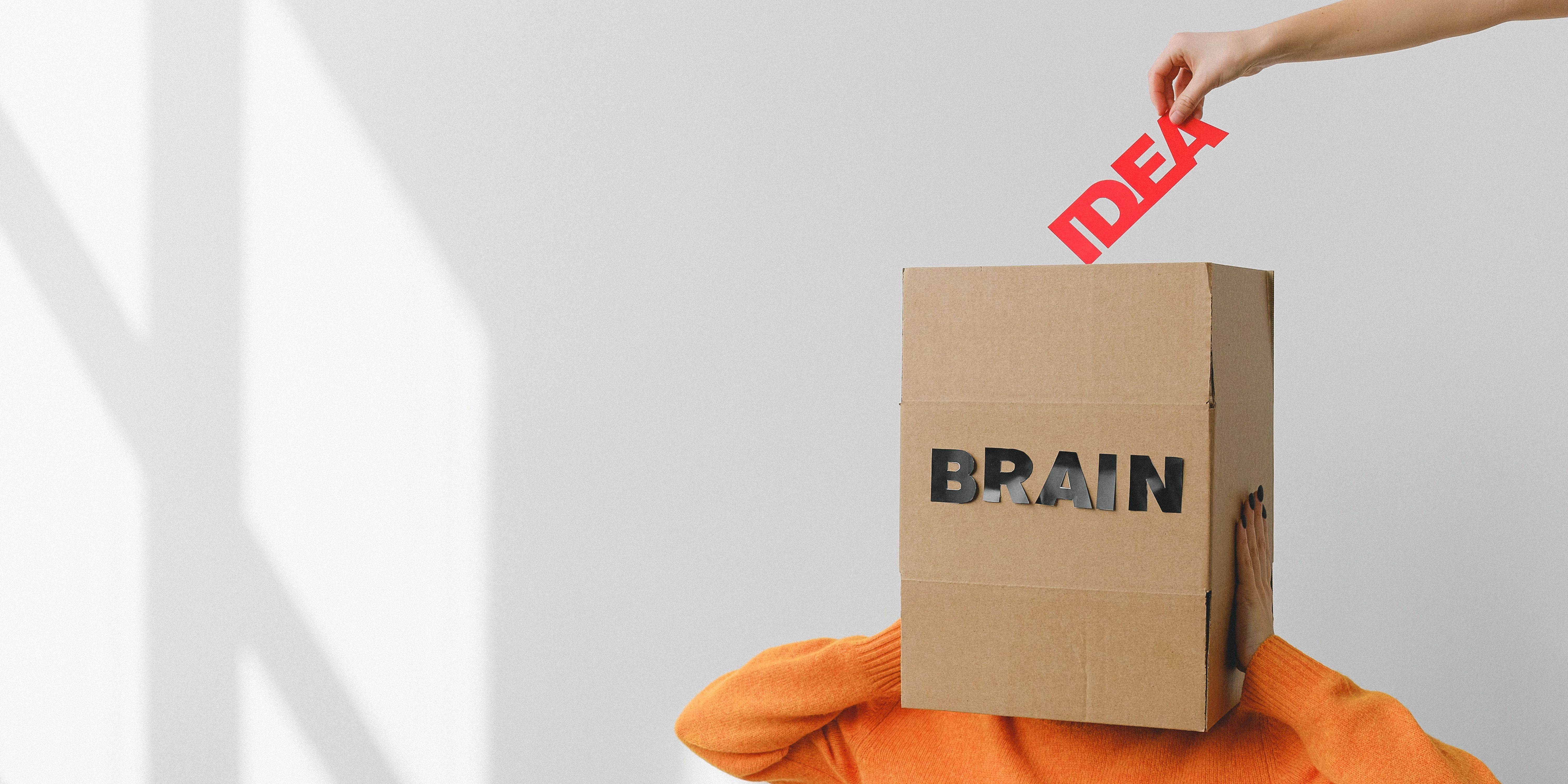 box labeled brain covering person's head while a hand drops the word 