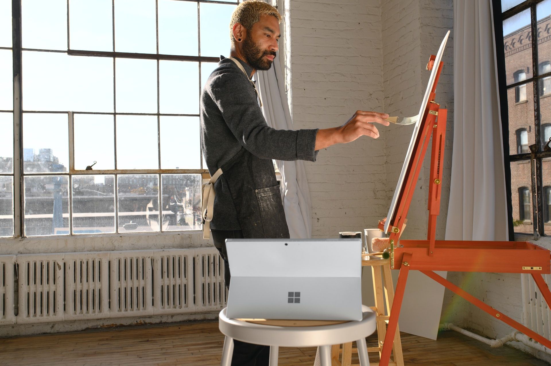 A picture of an artist painting on an easel with a Surface laptop next to them