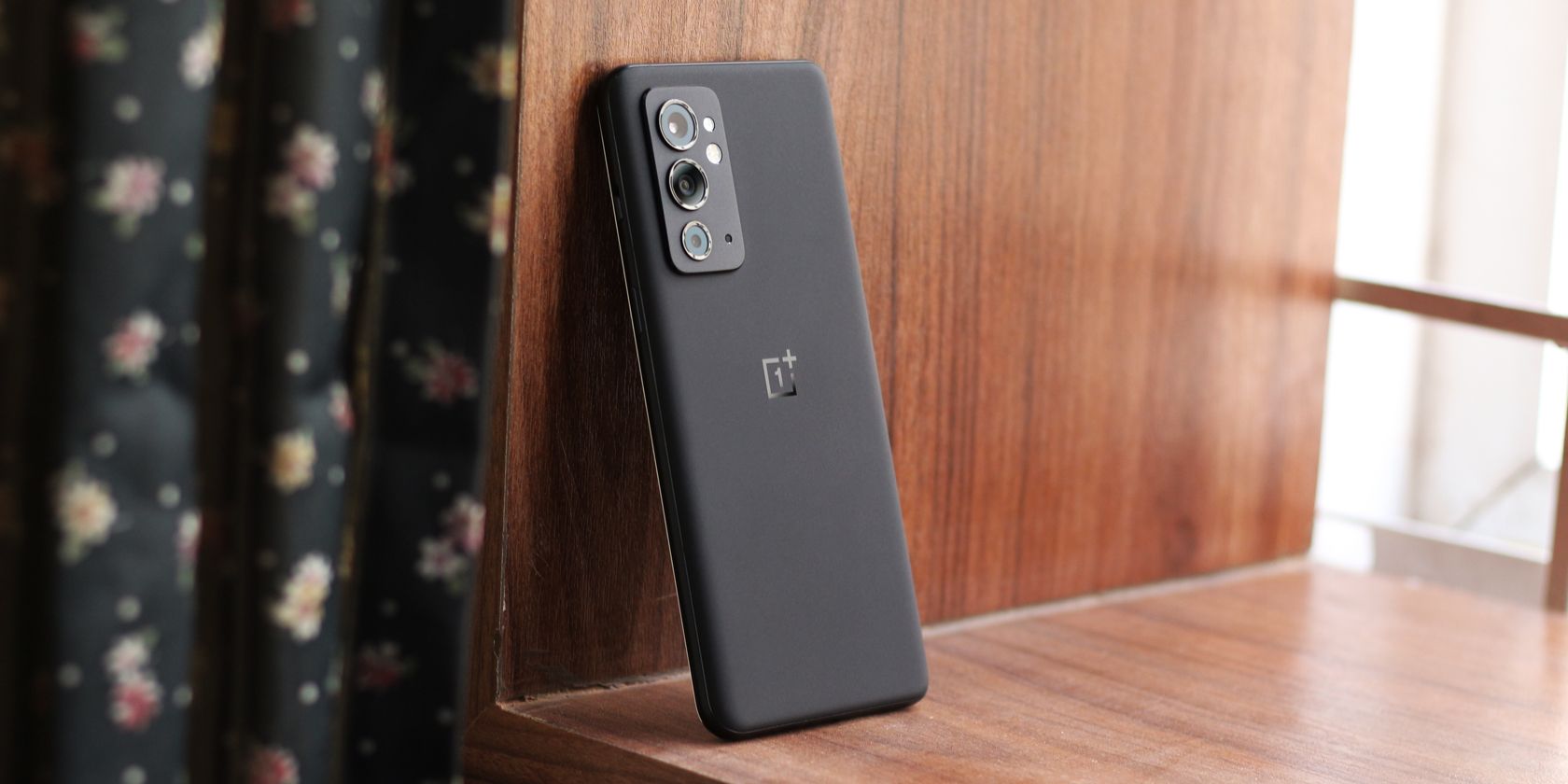 A black OnePlus phone propped up against a wooden frame