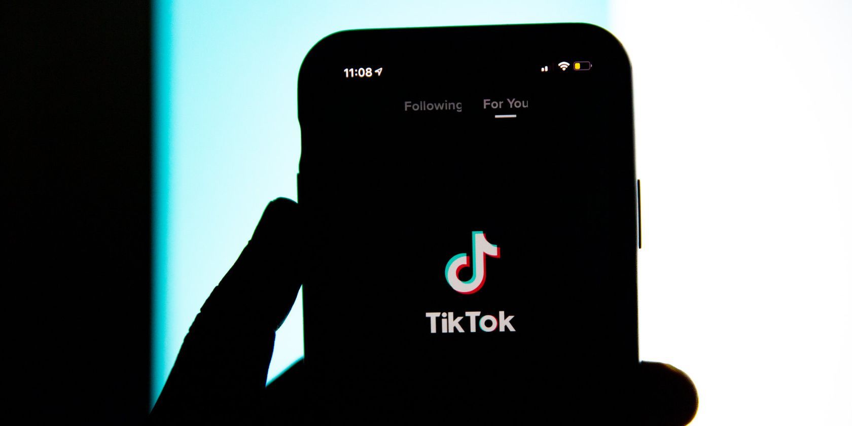 شخصی در اتاق تاریک گوشی را با برنامه tiktok باز در دست دارد