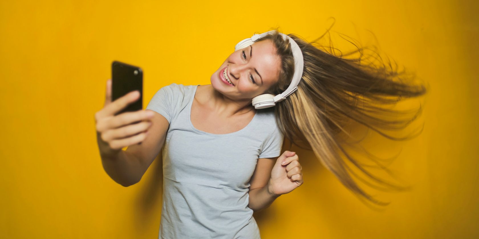 woman in headphones dancing while holding a phone