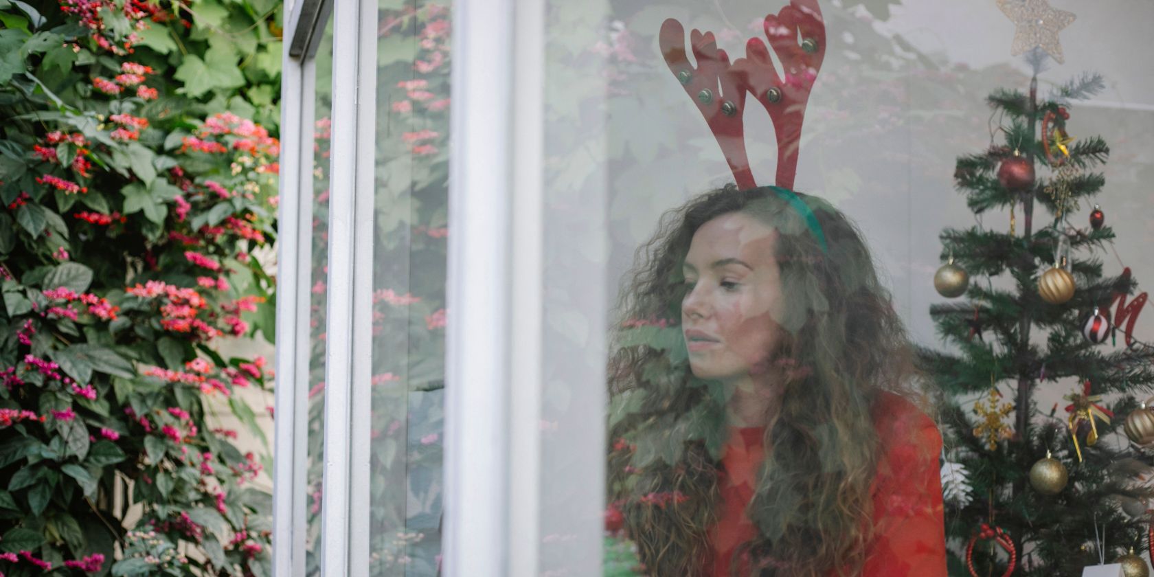a lady looks pensively through a window at Christmas time