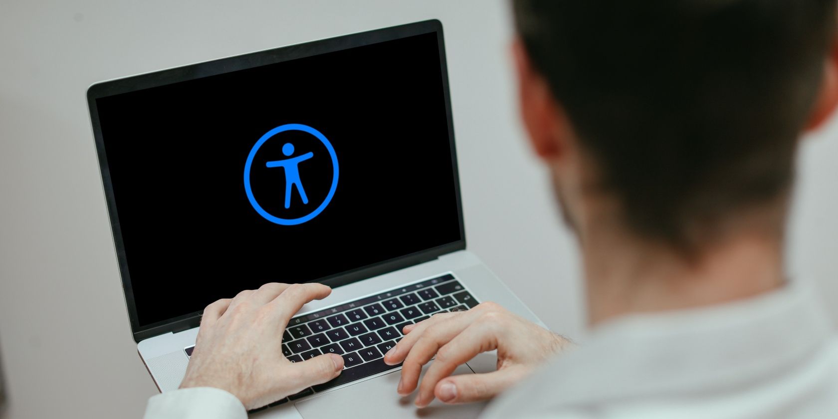 A man using a MacBook with an accessibility icon on the screen